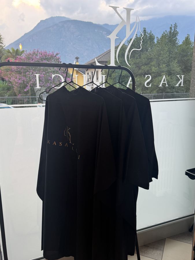 Mantelle nere con il logo Kasa Luci davanti alla vetrina con le montagne