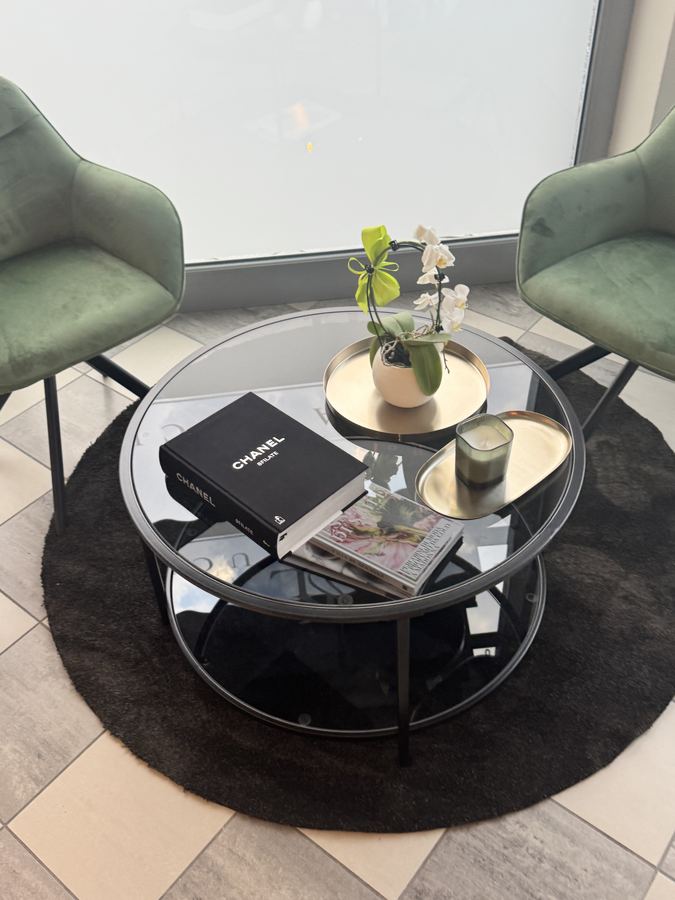 Tavolino in vetro con orchidea e riviste tra due poltroncine verdi